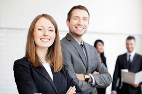 Mujer con saco negro junto a hombre con saco gris y al fondo una mujer y un hombre con saco negro