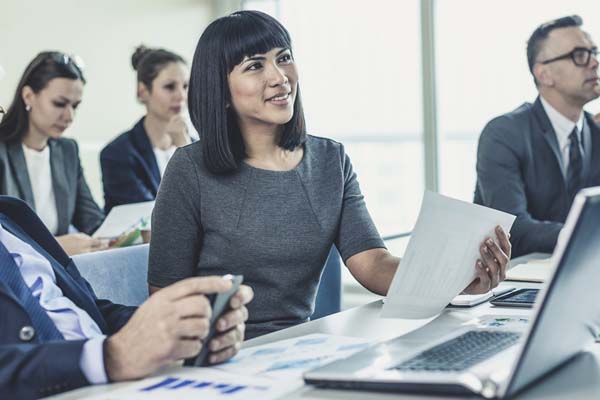 Mujeres y hombres sentados frente a mesas con laptops y hojas