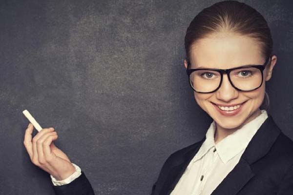 Mujer con saco negro y blusa blanca utilizando lentes y con un gis en la mano
