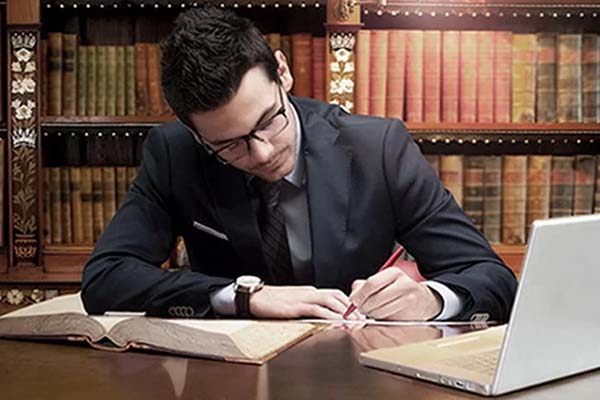 Hombre con traje negro sentado frente a un escritorio escribiendo en hojas blancas