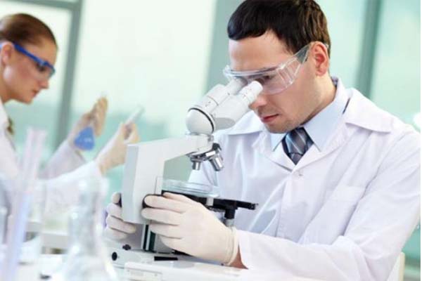 Hombre con bata blanca y guantes blanco mirando a través de un microscopio