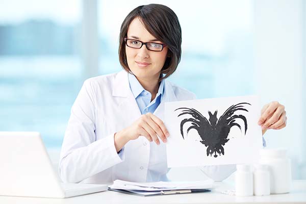 Mujer con bata blanca sentada usando lentes sosteniendo una hoja con una imagen en negro