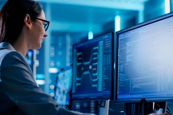 Mujer con saco azul usando lentes sentada frente a una computadora