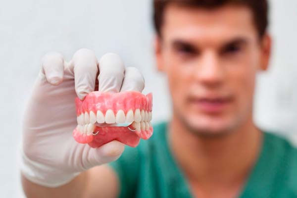 Hombre con bata verde y guantes blancos sosteniendo una dentadura