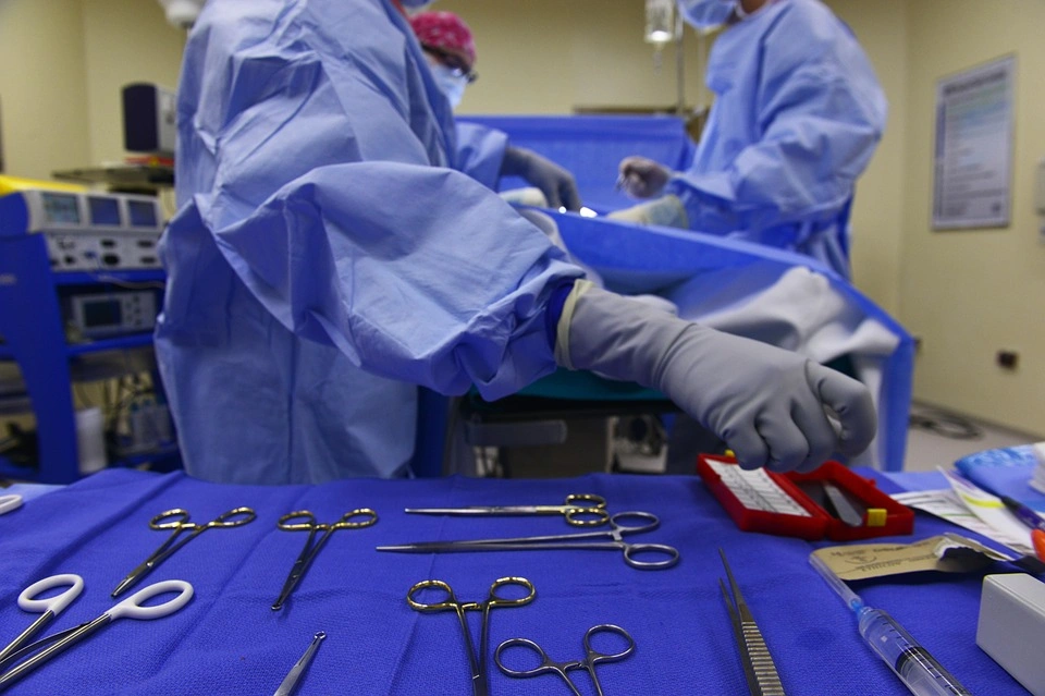 Herramientas de cirujia sobre una mesa con una tela en color azul y al fondo 3 personas médico cirujano.