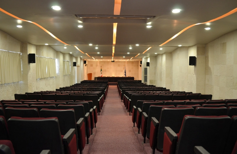 Auditorio con luces, cortinas, bocinas negras y sillas en color negro con vino , mesa y banderas al fondo