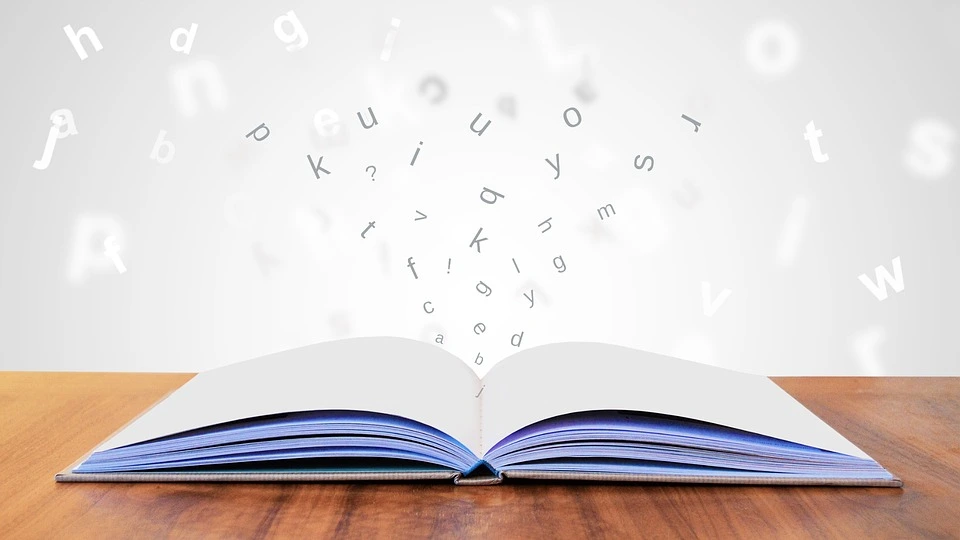 Libro blanco sobre una mesa con letras saliendo de el
