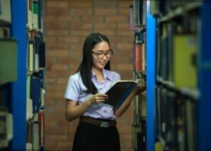 Mujer con blusa lila y falda negra en una biblioteca de preparatoria en Acapulco, sosteniendo un libro en las manos.