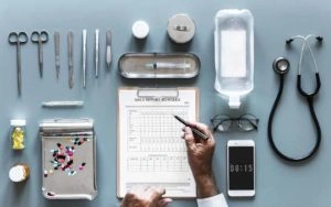 Hojas y pastillas con diferentes instrumentos de un médico sobre una mesa.