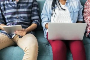 Mujer sentada con una laptop en las piernas y hombre sentado con una tablet en las manos.