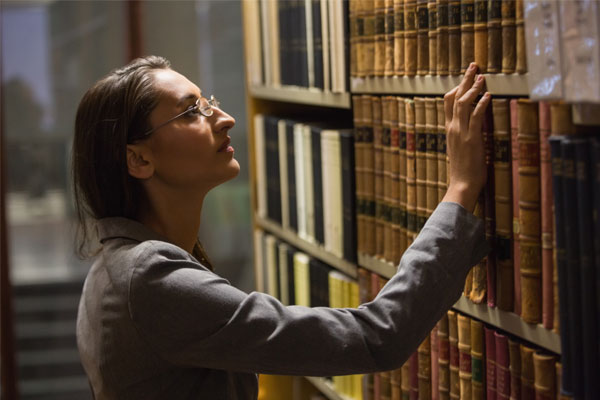 Mujer en busca de un libro en biblioteca que le permita conocer, abordar criterios reflexivos y analíticos.