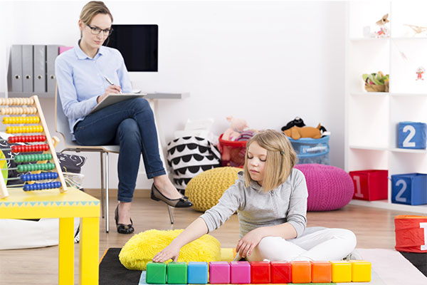 Psicóloga enfocada en el análisis a una niña que está realizando actividades con cubos de colores de manera didáctica.