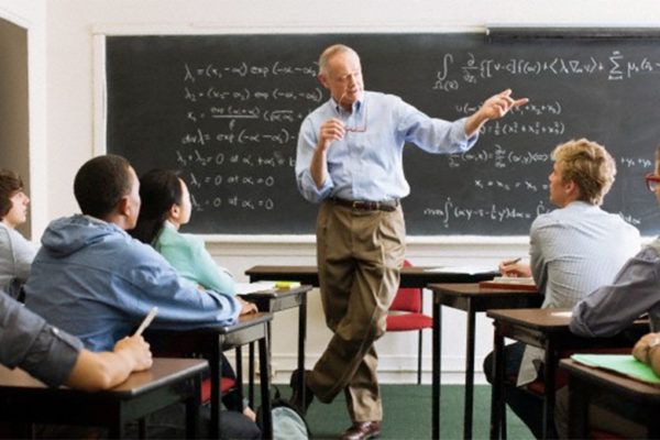 Profesor de cálculo sosteniendo lentes dando explicación sobre integrales. Alumnos poniendo atención.