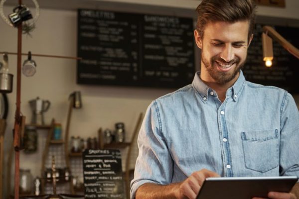 Hombre utilizando una tablet en cafetería sonriendo.